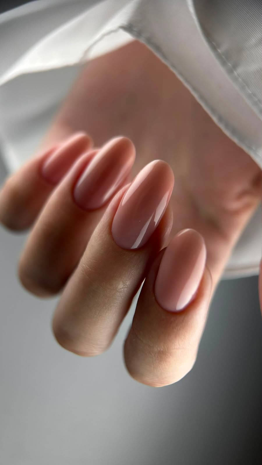 Glanzende nude amandelvormige nagels tegen witte zijde
