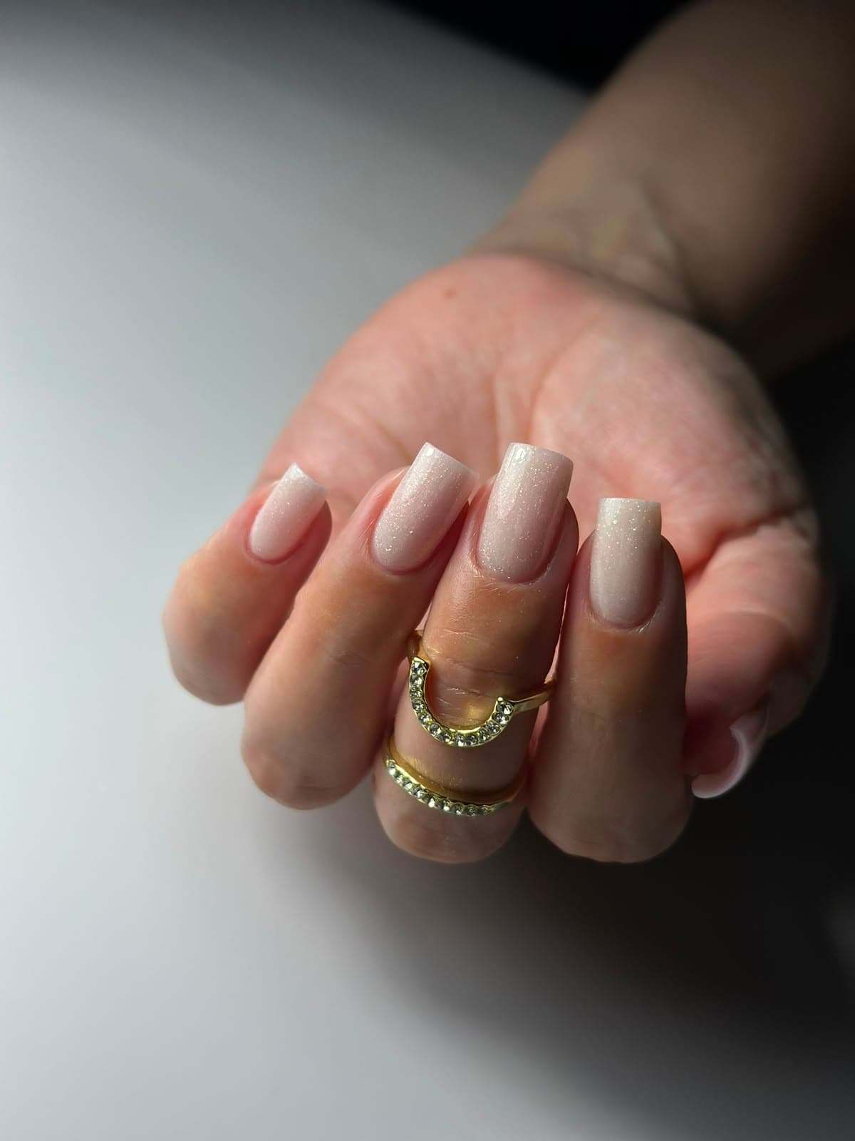 Parelmoerwitte nagels met fijne glitter en gouden ringen